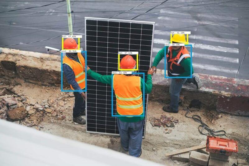 Three people wearing hard hats and safety vests installing a solar panel.
